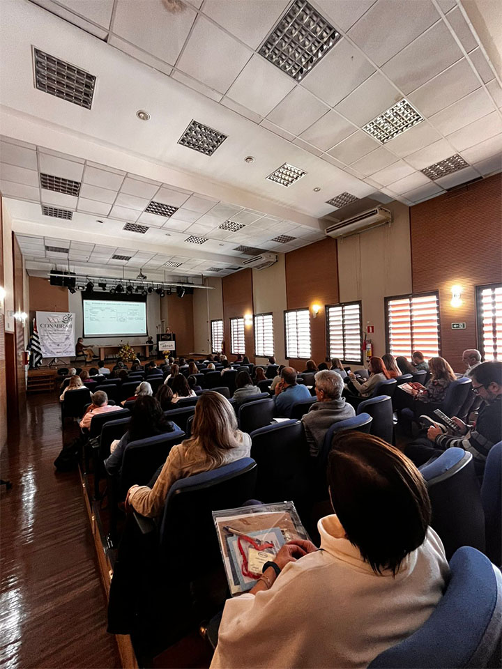 #ParaTodosVerem Fotografia panorâmica no anfiteatro do HSPM. Na foto, vemos os participantes sentados, de costas, e, à frente, o palestrante realizando a apresentação.