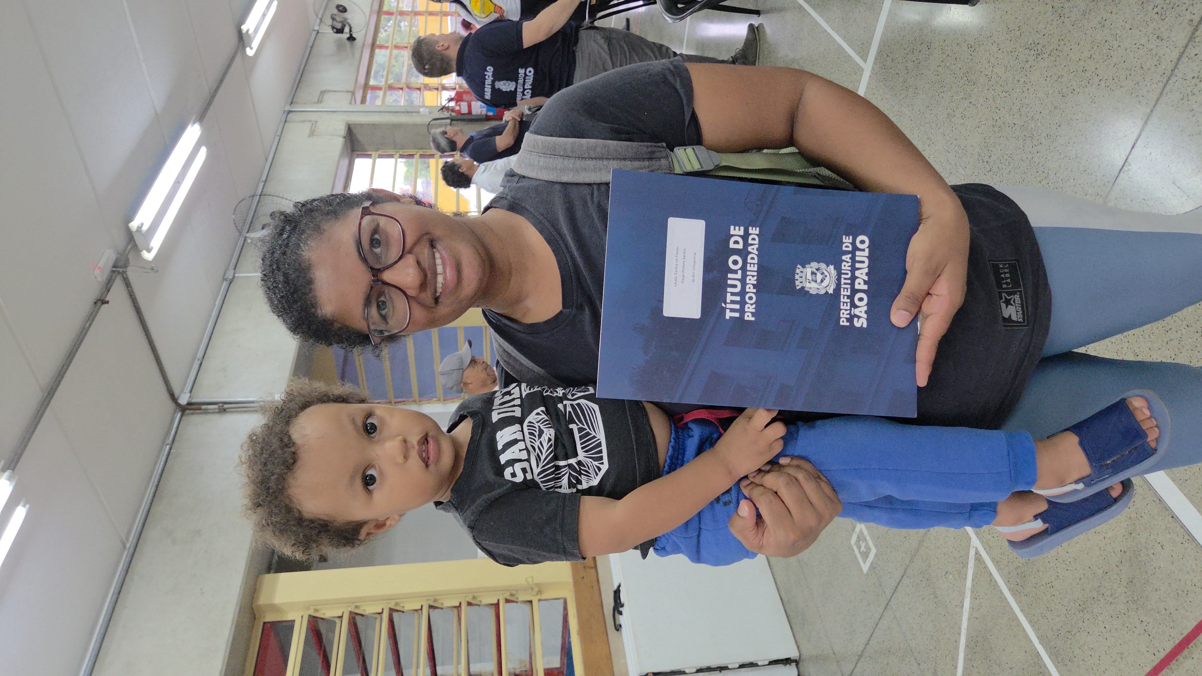 Mulher com seu filho segura a matrícula de sua casa