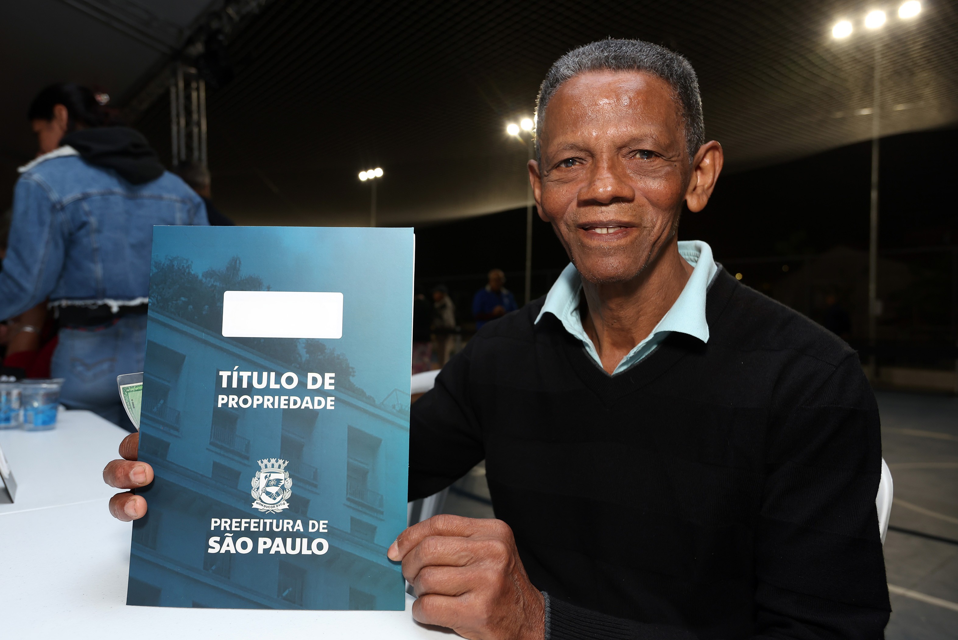 Um homem de terceira idade segurando uma pasta azul escrito 