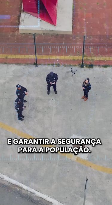 A imagem apresenta uma cena vista de cima, provavelmente capturada por um drone ou câmera aérea.  Há quatro pessoas no centro da imagem: três delas usam uniformes escuros, possivelmente policiais ou agentes de segurança, enquanto a quarta pessoa está com roupas civis, incluindo um casaco e botas marrons.