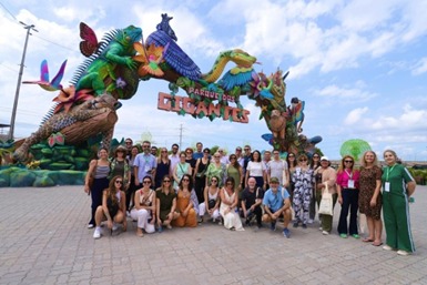 A imagem é uma foto de grupo com grande número de pessoas, provavelmente em uma visita, em frente a uma entrada ou portal temático muito elaborado. O portal é colorido com a imagem de alguns animais, escrito em letras grandes Parque dos Gigantes.