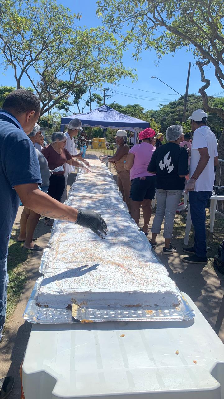Em meio a Praça na avenida dos Metalúrgicos, sob uma tenda e sobre mesas plásticas brancas enfileiradas está o bolo de 42 metros. Nas laterais os cozinheiros enfeitam o bolo com cobertura e confetes.