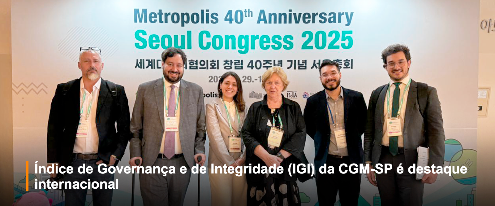 Foto de seis pessoas posando na frente do Banner do evento